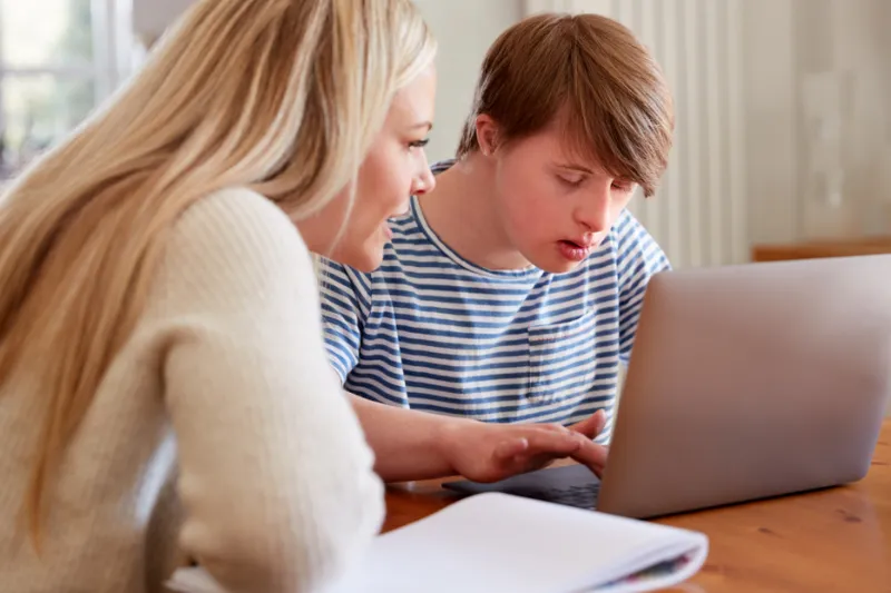 Nachhilfelehrerin unterstützt beeinträchtigten Schüler am Laptop durch Nachhilfe